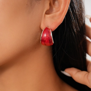 Close-up of red resin geometric C-shaped earrings with silver edging on a model