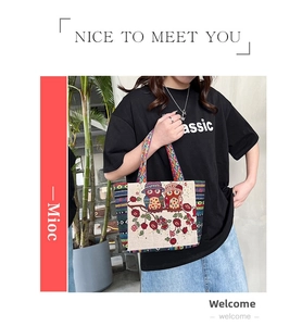 Detailed embroidery of two owls on a floral branch upon a beige canvas tote bag