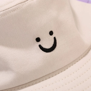 Close-up of black smiley face embroidery on beige cotton twill bucket hat fabric