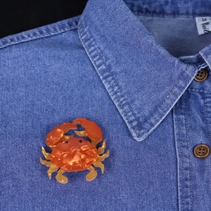 Artistic acrylic crab brooch with orange and yellow gradient on a denim shirt collar