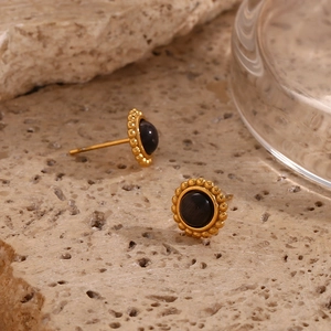Detail of 18K gold plated sunburst earrings with black opal on a stone surface