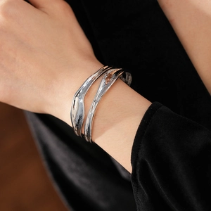 Detailed view of silver organic wavy layered open cuff bracelet on a female wrist
