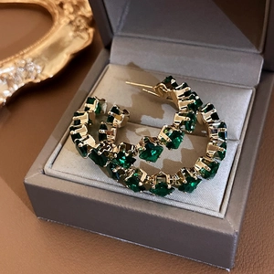 Detailed shot of emerald rhinestones set in golden hoop earrings inside a jewelry box