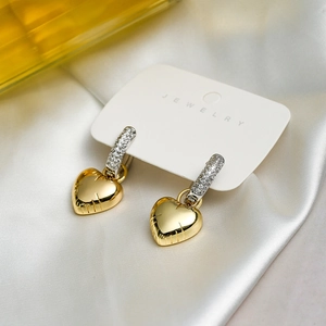 Detailed view of heart-shaped gold earrings with zircon studs on a white jewelry card