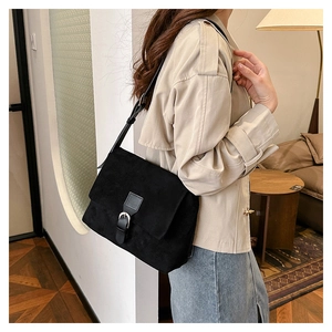 Side view of a matte black suede shoulder bag with a silver buckle on a model
