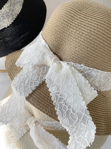 Close-up of woven straw sun hats with elegant white lace ribbons and bow details