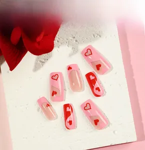 Detail view of pink French tip press-on nails with red heart designs on marble background