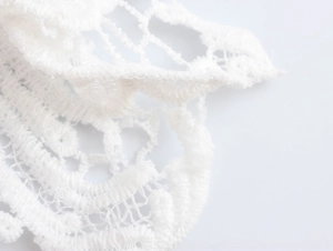 Gros plan sur la dentelle blanche et la texture ajourée de cette élégante robe mi-longue