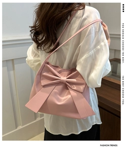 Close-up of pink PU leather shoulder bag with a large bow detail on a model