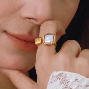 Golden open ring with square pearl detail shown on a finger in high quality close-up