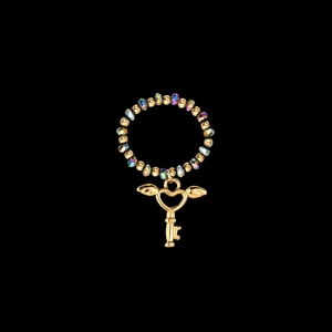Detail of beaded ring featuring a golden heart key charm with wings on black background
