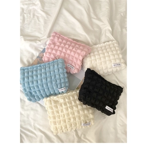 Detail showing five bubble-textured makeup bags in assorted candy colors on white linens