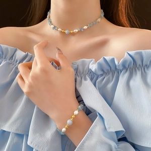 Gros plan du collier en aigue-marine et perles blanches sur un modèle en haut bleu