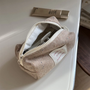 Detailed shot of beige herringbone tweed makeup bag with colorful flecks and hair clip