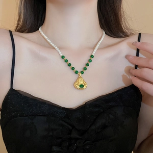 Detail of a golden Maitreya Buddha pendant with green gemstone on a pearl necklace