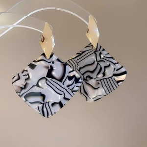 Detail of geometric earrings with gold studs and black and white marbled pendants