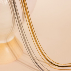 Three-layer gold and silver stacked snake chain necklace on minimalist white ceramic vase