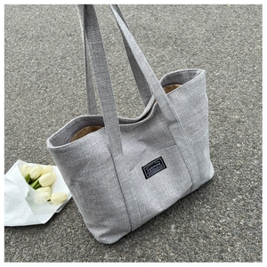 Detail shot of textured grey canvas tote bag showing the front pocket and quality label