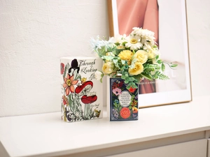 Detail view of book-shaped ceramic vases with floral prints and literary quotes on top