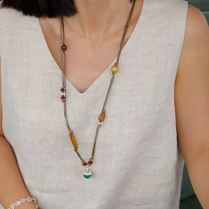 Détail d'un collier bohème avec pendentif vert et perles en bois sur le cou d'un modèle