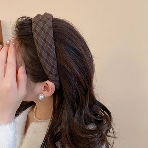 Detail shot of a brown plaid fabric headband styled on long wavy hair with pearl jewelry