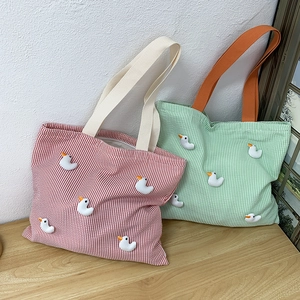 Detail of striped canvas tote bags with cute 3D duck dolls on a wooden surface