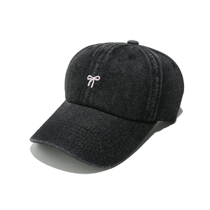 Close-up of pink bow embroidery on black denim baseball cap with washed fabric texture