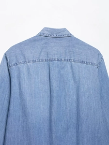 Detailed back view of a light blue denim shirt showing the yoke and pleated back stitching