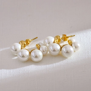 Detailed view of elegant gold hoop earrings featuring alternating white pearls on textured surface