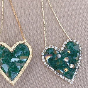 Macro detail of emerald green heart-shaped crystal earrings with gold trim and rhinestones