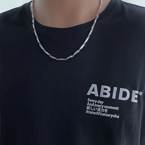 Gros plan d'un collier chaîne en acier inoxydable argenté porté sur un t-shirt noir