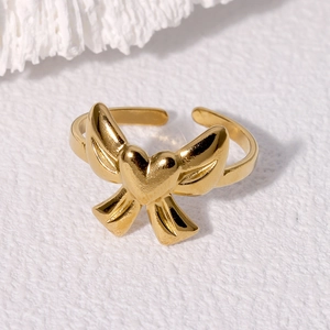 Detail view of 18K gold plated heart bow ring with adjustable open band on stone surface