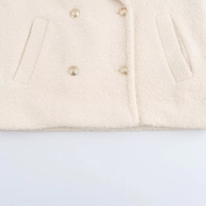 Detail of cream double-breasted coat featuring embossed gold buttons and wool-like texture