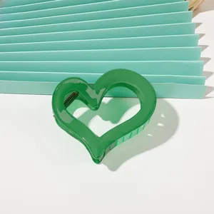 Detail shot of a green heart-shaped hair claw clip on a decorative paper fan background