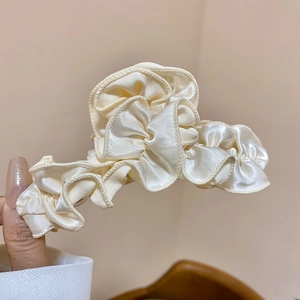 Close-up of ruffled cream satin fabric texture on a large hair claw clip for women
