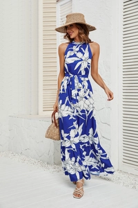 Robe d'été dos nu bleue à fleurs blanches présentée dans un décor de vacances ensoleillé