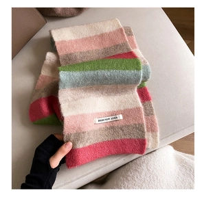 Close-up of rainbow striped mohair scarf texture and brand tag on soft grey sofa