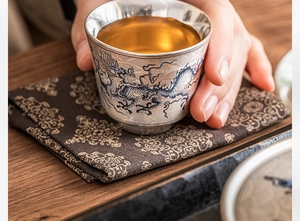 Primer plano de una taza de té plateada con motivos de dragón azul y té ámbar
