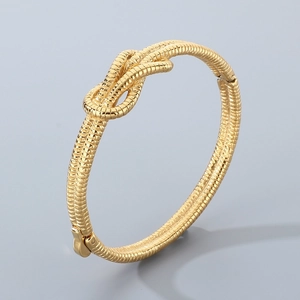 Close-up detail of golden knot bracelet showing intricate woven texture and metallic finish