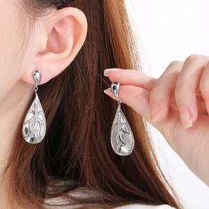 Close-up of silver teardrop drop earrings with intricate mesh texture and sparkling zircons