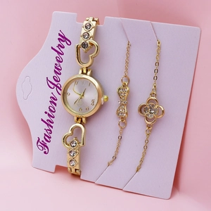 Close-up of gold quartz watch and bracelets set with heart and clover charms on pink card