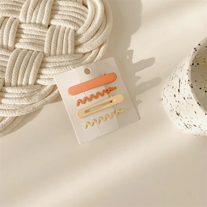 Detail view of 4-piece matte metal hair clips in orange and beige on a display card