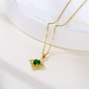 Elegant gold clover necklace with green crystal square pendant on marble tray