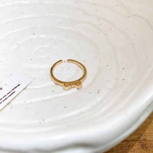 Close-up of a delicate golden bow open ring on a textured white ceramic plate