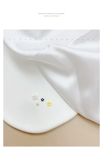 Macro detail of 3D resin flower nail charms with gold beads on white silk background