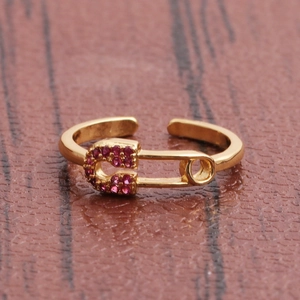 Gold safety pin adjustable ring with pink cubic zirconia on a rustic wood surface