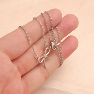 Close-up of a silver bow pendant on a delicate chain held against a pink background