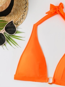 Flat lay of vibrant orange halter bikini top with bow tie and resin ring detail