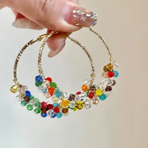 Gros plan de grandes créoles en fil doré et perles de cristal multicolores facettées