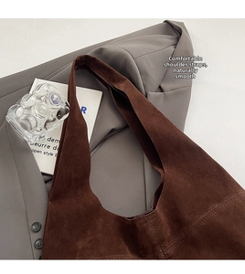 Close-up of brown suede tote bag with wide shoulder strap on grey blazer fabric